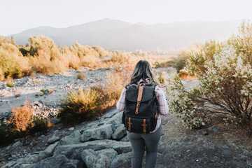 Unrecognizable woman with a backpack on and a pale pink blouse in nature.