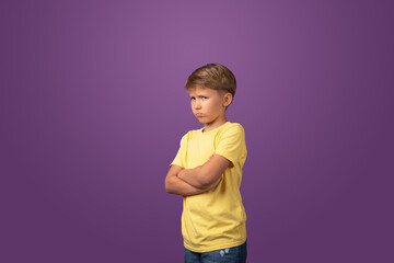 Studio shot of offended preteen boy with arms crossed looking to camera while standing on purple...
