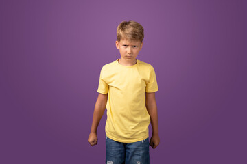Angry Caucasian preteen boy clenching fists and looking at camera with aggressive face expression while standing on purple background. Studio shot.