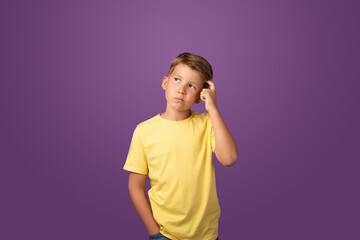 Thoughtful preteen kid boy standing with puzzled serious expression, making choise thinking against purple background. Studio shot