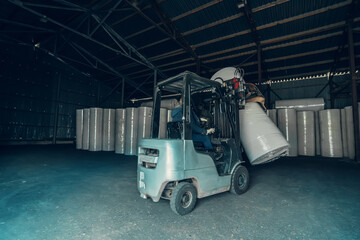 Forklift transports large roll of paper at recycling and toilet paper manufacturing plant.