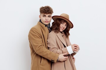 a man and a woman pose on a white background in an autumn coat and sweaters. the guy is standing next to the girl holding her hand and pressing a little to himself