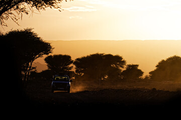 A car silhouette riding through dusty desert route in the evening. Setting sun in the background...