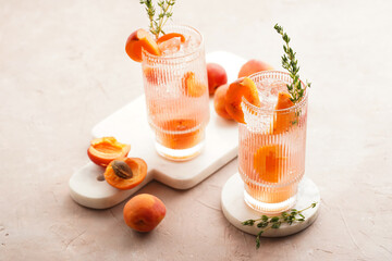 Two glasses with refreshing summer cocktail with ice cubes, apricot slices and fresh thyme on marble board on pale purple background