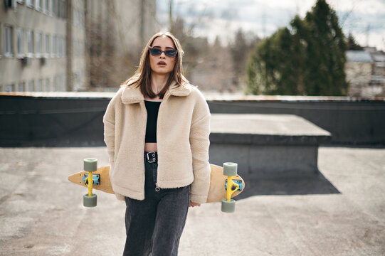 Beautiful woman with skateboard standing on building rooftop