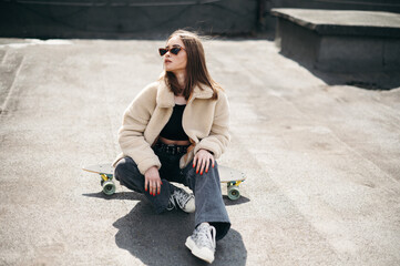 Woman sitting on skateboard and posing on camera outdoors