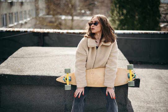Pretty woman sitting with skateboard on sunlight rooftop