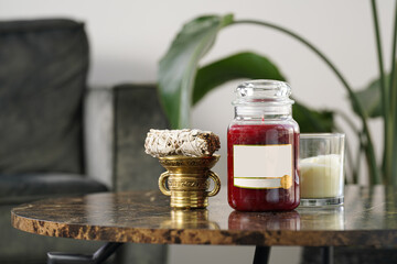 Mock up in interior: blank off-white and crimson pillar candle in glass jar with label and silver...