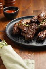 Traditional south european skinless sausages cevapcici made of ground meat and spices on black plate on dark wooden board, with thyme