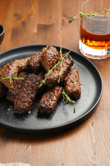 Traditional south european skinless sausages cevapcici made of ground meat and spices on black plate on dark wooden board, with thyme