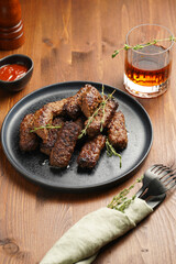 Traditional south european skinless sausages cevapcici made of ground meat and spices on black plate on dark wooden board, with thyme