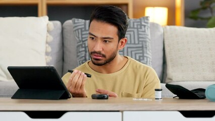 One Asian male with a chronic illness or disease pricking himself for a blood test. Man suffering from diabetes checking his sugar levels with a home test kit and digital tablet in the living room.