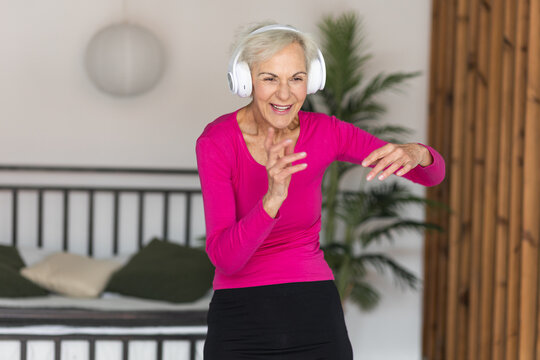 Beautiful senior woman with short grey hair and lovely smile listening to music and dancing at home . Concept of attractive good looking elderly female, mature women with active lifestyle.
