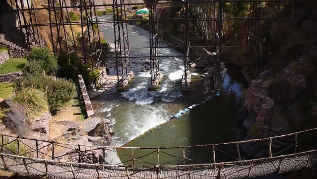 moving river under distant metal bridge with trees, checacupe, cusco, peru