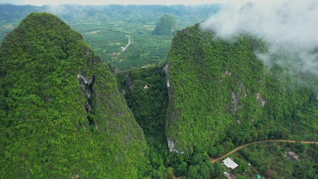 Aerial view over the temple (Tham Nam Lod Cave Temple) Beautiful Buddha statue on the hill. Chumphon province, Thailand. clouds and mountains in the morning. drone. 4k
