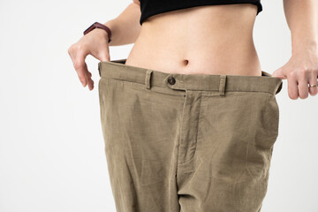 Slim sporty woman in beige pants showing a result of weight loss on white background. Diet concept and weight loss.