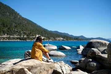 Woman is sitting on the rock at Lake Tahoe. Travel and explore America for the beautiful view and...