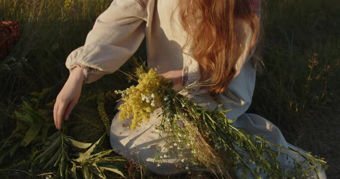 A girl in a Ukrainian embroidered dress weaves a wreath of wild flowers