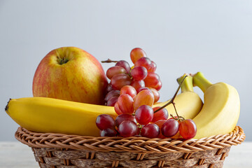 Ripe fruits in wicker basket on gray background. Harvest concept. Bananas, apples and grapes.