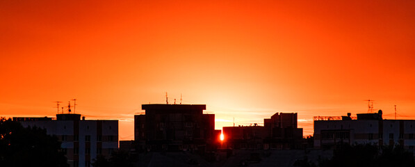 Silhouette of city at sunset. Sun is rising over tall buildings. Dramatic sky in sun rays. Urban landscape at dawn. Copy space, banner format.