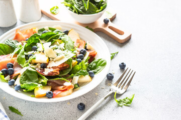 Healthy salad with spinach, arugula, jamon, pear, blueberry and parmesan on white background.