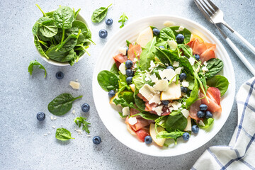 Salad with jamon, green leaves, pear and blueberry. Top view on white background.