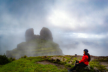woman in red with a hat observing the waqrapucara archaeological rest on a foggy morning