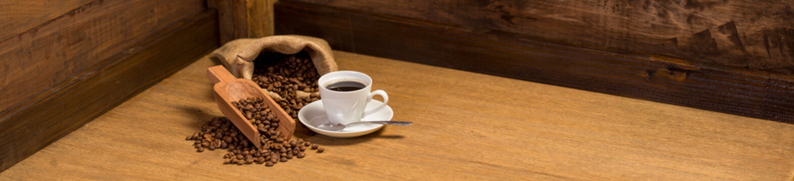 cup of coffee with bag and spoon full of beans on wooden background. panoramic image with copy space.