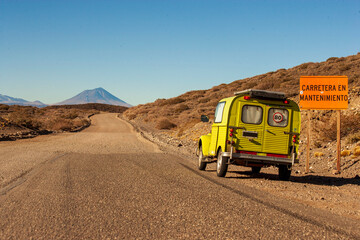 Old yellow car on the pavement road. The letters with CARRETERA EN MANTENIMIENTO mean CARRETERA EN MANTENIMIENTO