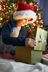 Obraz na płótnie Canvas A cute boy opens a gift near the New Year tree. Christmas miracle