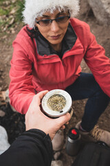 mujer latina calentando agua en cocina portatil y haciendo mates a la vera del rio 