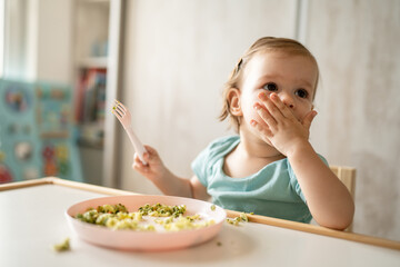 one girl small caucasian child one year old eat at the table at home