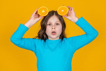 Fototapeta na wymiar shocked teen girl hold orange fruit on yellow background