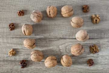Circle of whole walnuts and peeled seeds on brown wood textured background, copy space