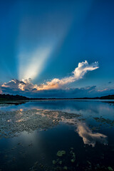 Naklejka na ściany i meble Vertical Image of Sunset over tranquil water with cloud that looks like a dragon and sunbeams