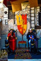 king and queen sitting on a throne with 2 dogs next to them and their shield of a lion