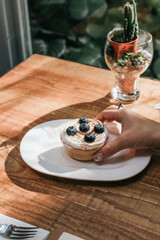Hand pick up Lemon meringue and blueberry tart in white plate on wooden table. Pie Dessert. Horizontal Copy space