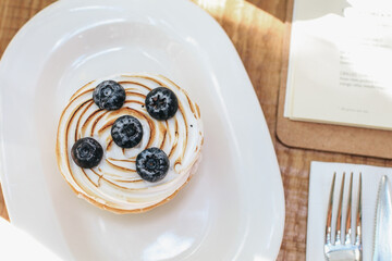Lemon meringue and blueberry tart in white plate on wooden table. Pie Dessert. Horizontal Copy space - obrazy, fototapety, plakaty