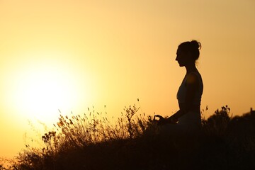 Silhouette of woman meditating outdoors at sunset. Space for text