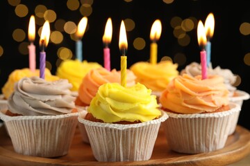 Tasty birthday cupcakes on wooden stand against blurred lights, closeup