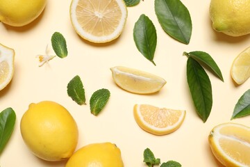 Many fresh ripe lemons with green leaves and flower on beige background, flat lay