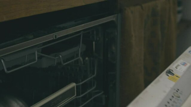 Detail of two hands opening a dishwasher, inserting a bowl and having a wash done