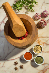 Top view of large wooden mortar and pestle with colorful spices.