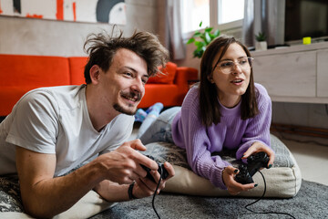 Man and woman lying on the floor at home playing video game console