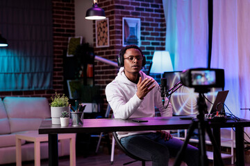 African american blogger recording live podcast vlog on camera, filming livestream in studio with neon lights. Social media influencer vlogging internet video as channel content.