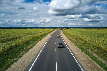 Aerial view of intercity road between green agricultural fields with fast driving cars. Top view from drone of highway traffic