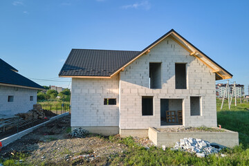 Aerial view of unfinished house with aerated lightweight concrete walls and wooden roof frame covered with metallic tiles under construction