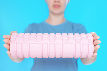 Young woman hold a massage foam roller on blue background close-up, selective focus.