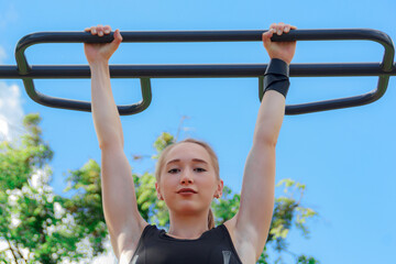 Fototapeta premium Young blonde woman in a dark tracksuit is engaged in fitness on the sports ground