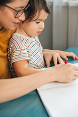 Fototapeta premium Mom with her boy are drawing with a pencils sitting at a table at home. Writing education concept.
